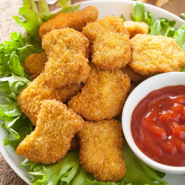 Crispy golden chicken nuggets on a bed of lettuce with a side of bright red ketchup.