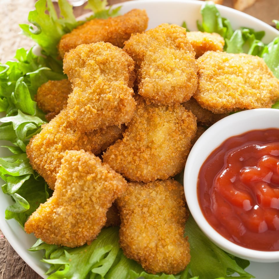 Crispy golden chicken nuggets on a bed of lettuce with a side of bright red ketchup.
