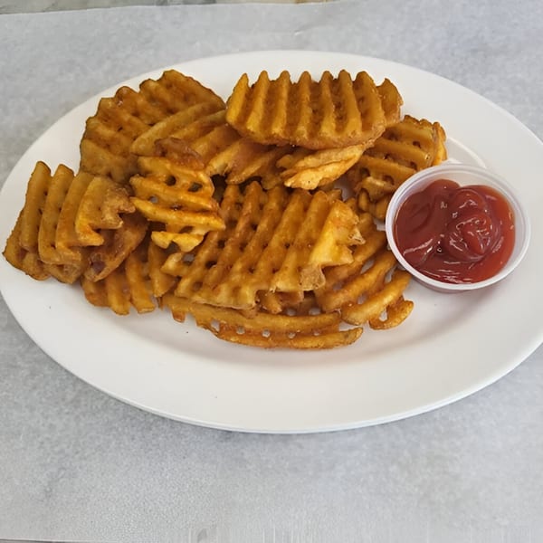 A white plate piled high with golden-brown waffle fries and a small cup of ketchup.