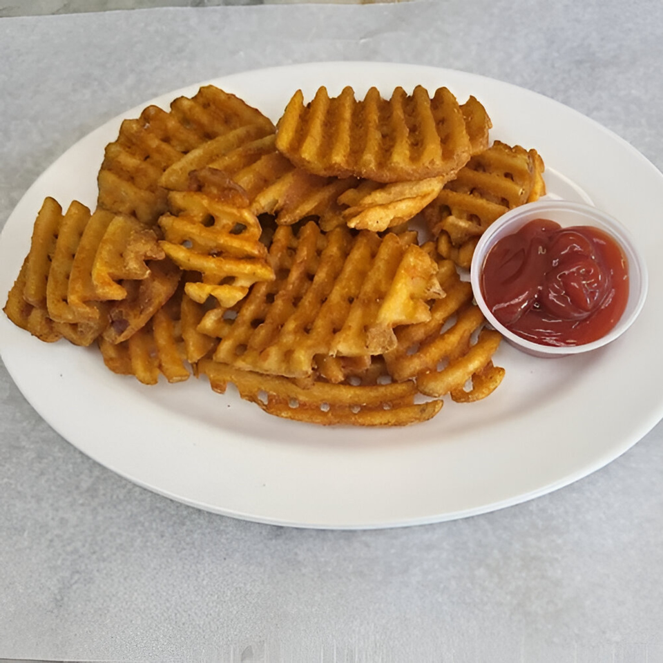 A white plate piled high with golden-brown waffle fries and a small cup of ketchup.