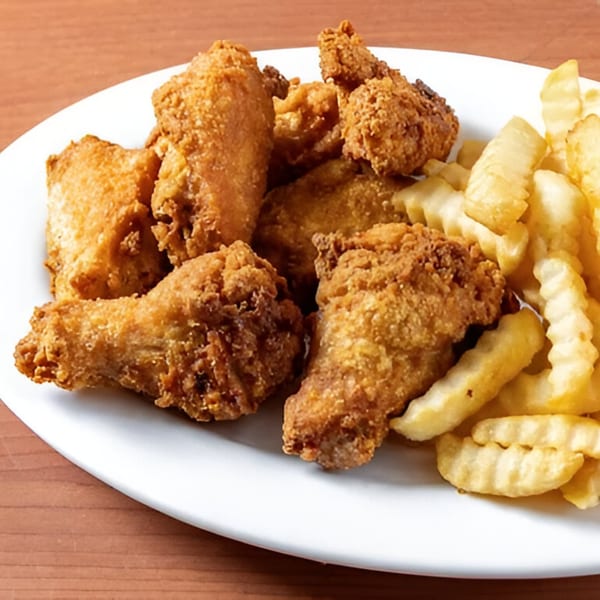 A white plate holds crispy fried chicken pieces and crinkle-cut french fries on a wooden table.