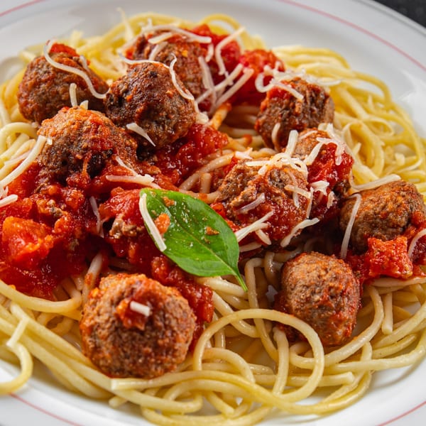 Spaghetti with meatballs, marinara sauce, shredded Parmesan, and a basil leaf on a white plate.