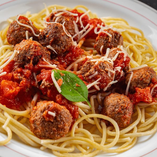 Spaghetti and meatballs with tomato sauce, parmesan cheese, and a basil leaf on a white plate.