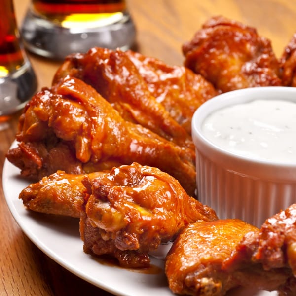 A plate of Bella Donna Pizzeria's buffalo wings with ranch dipping sauce and two glasses of beer.